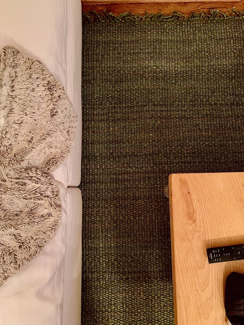 Green rug, white couch, wood table, gray blanket.